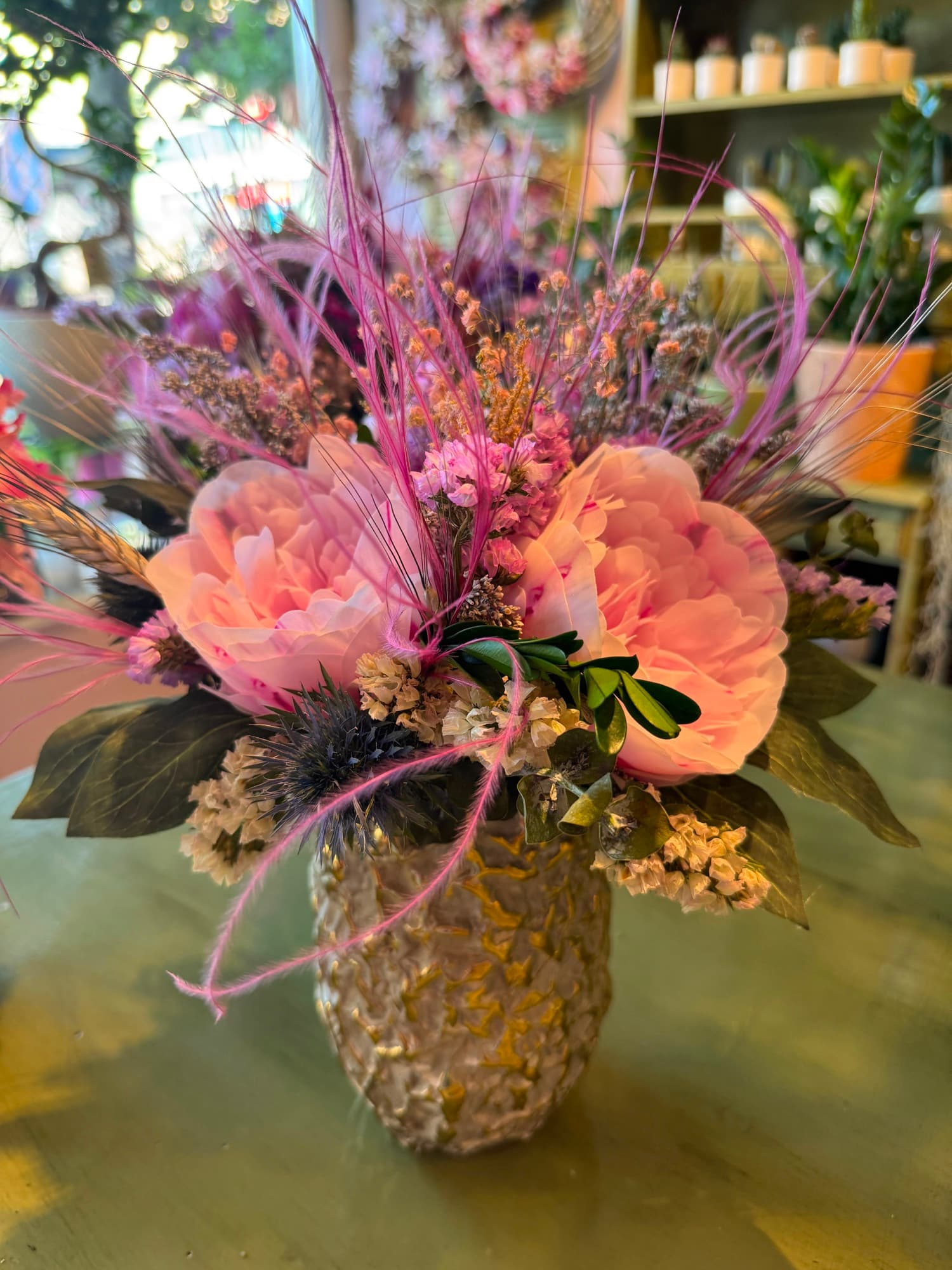 A dried arrangement in pink and peach tones in a gold vase