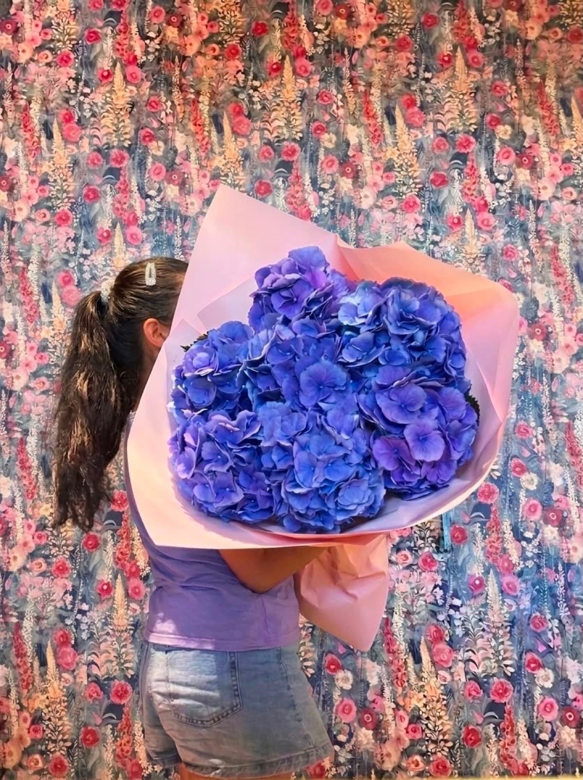 A blue hydrangea wrapped in paper in front of the tapestry